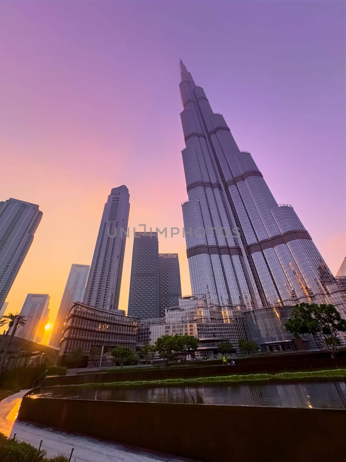 UAE, Dubai, 26 December 2024: The famous Burj Khalifa skyscraper at dusk, Dubai's sights during the incredible sunset sky, skyscrapers illuminated at night, pink sky, palm trees. High quality photo