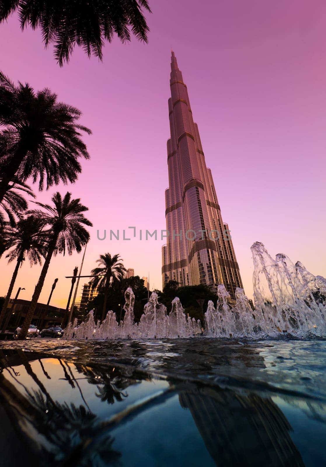 UAE, Dubai, 10 December 2024: The famous Burj Khalifa skyscraper at dusk, Dubai's sights during the incredible sunset sky, skyscrapers illuminated at night, pink sky, palm trees. High quality photo