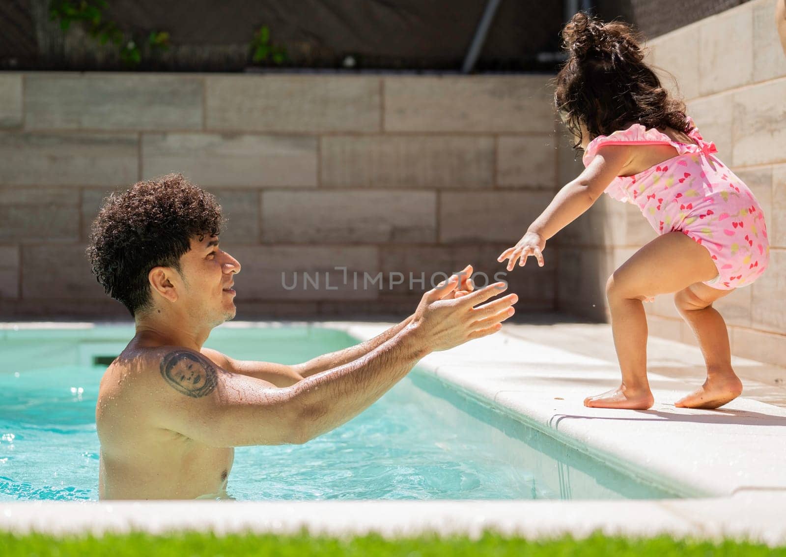 Dad catching daughter jumping in swimming pool during summer holidays.