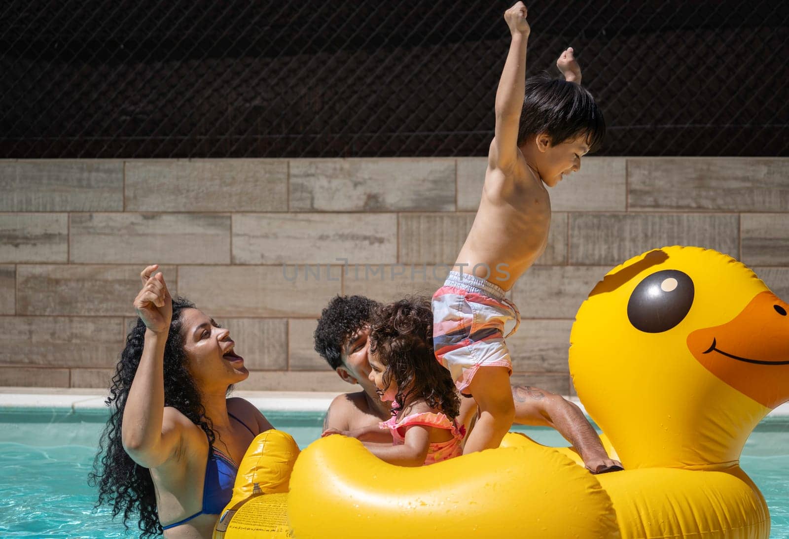 Excited family playing on inflatable duck float in swimming pool, enjoying summer vacation.