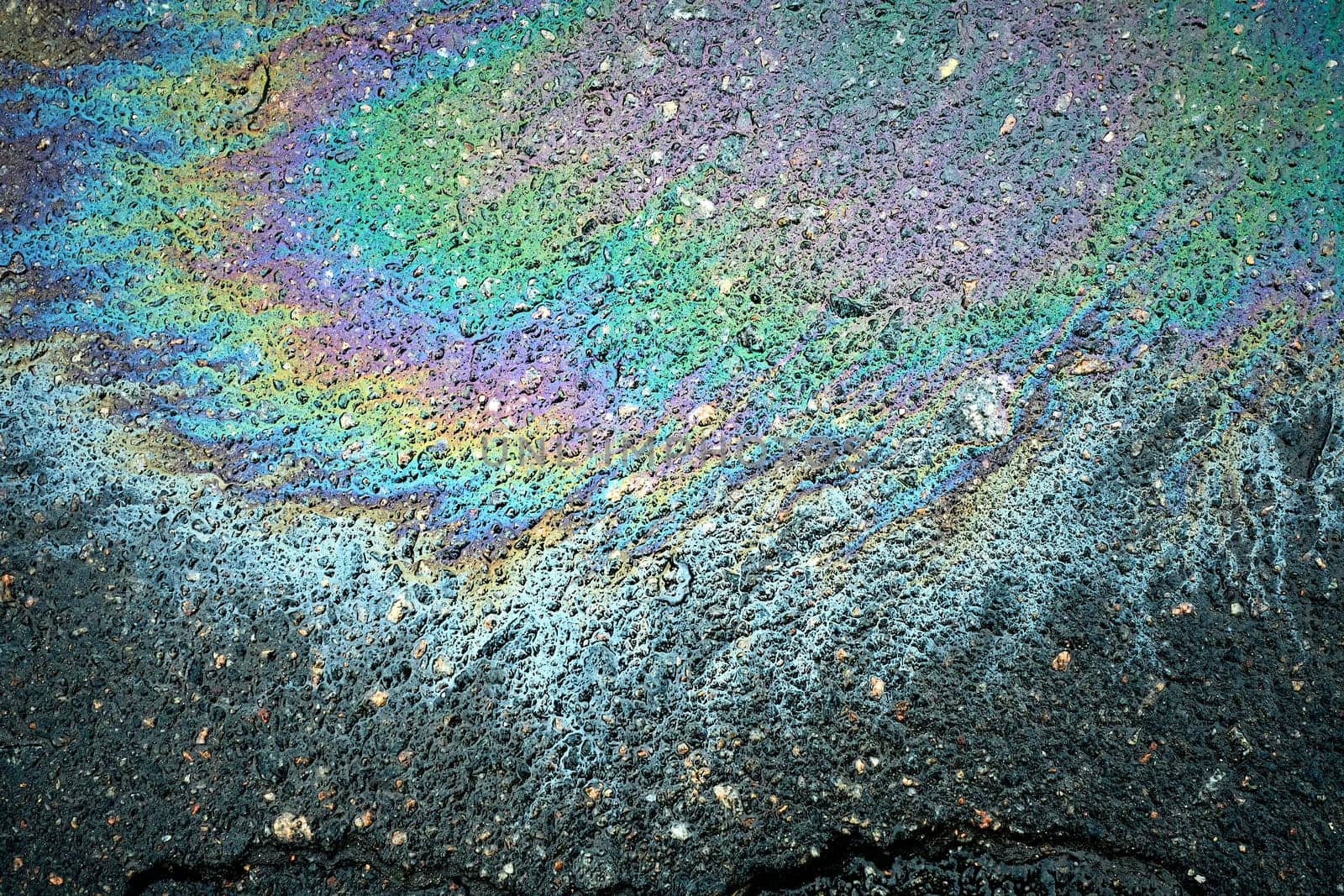 Petrol spill on asphalt creating a textured abstract design, showcasing the colors of motor oil and gas
