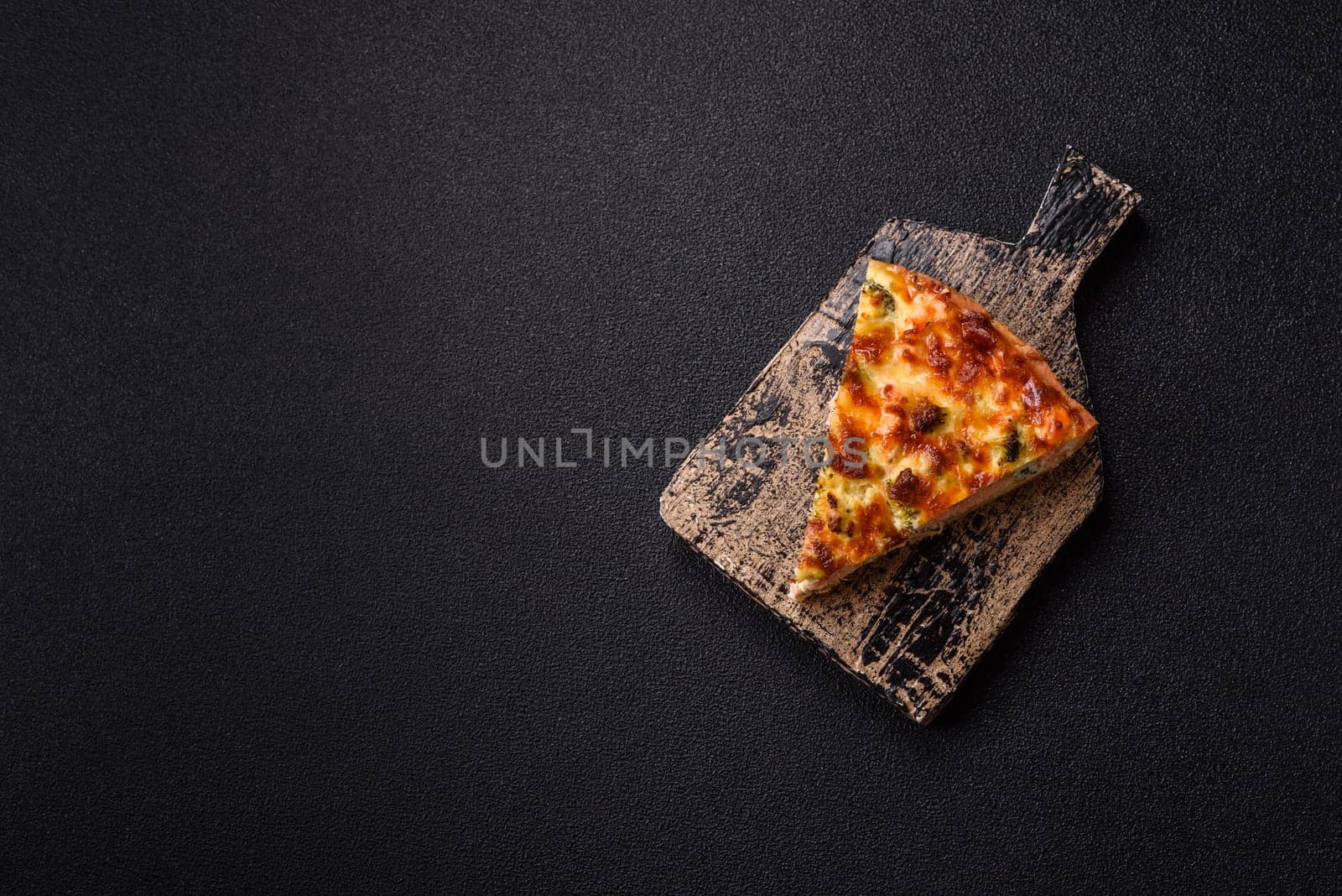 Delicious fresh quiche with broccoli, cheese, spices and herbs cut into pieces on a dark concrete background