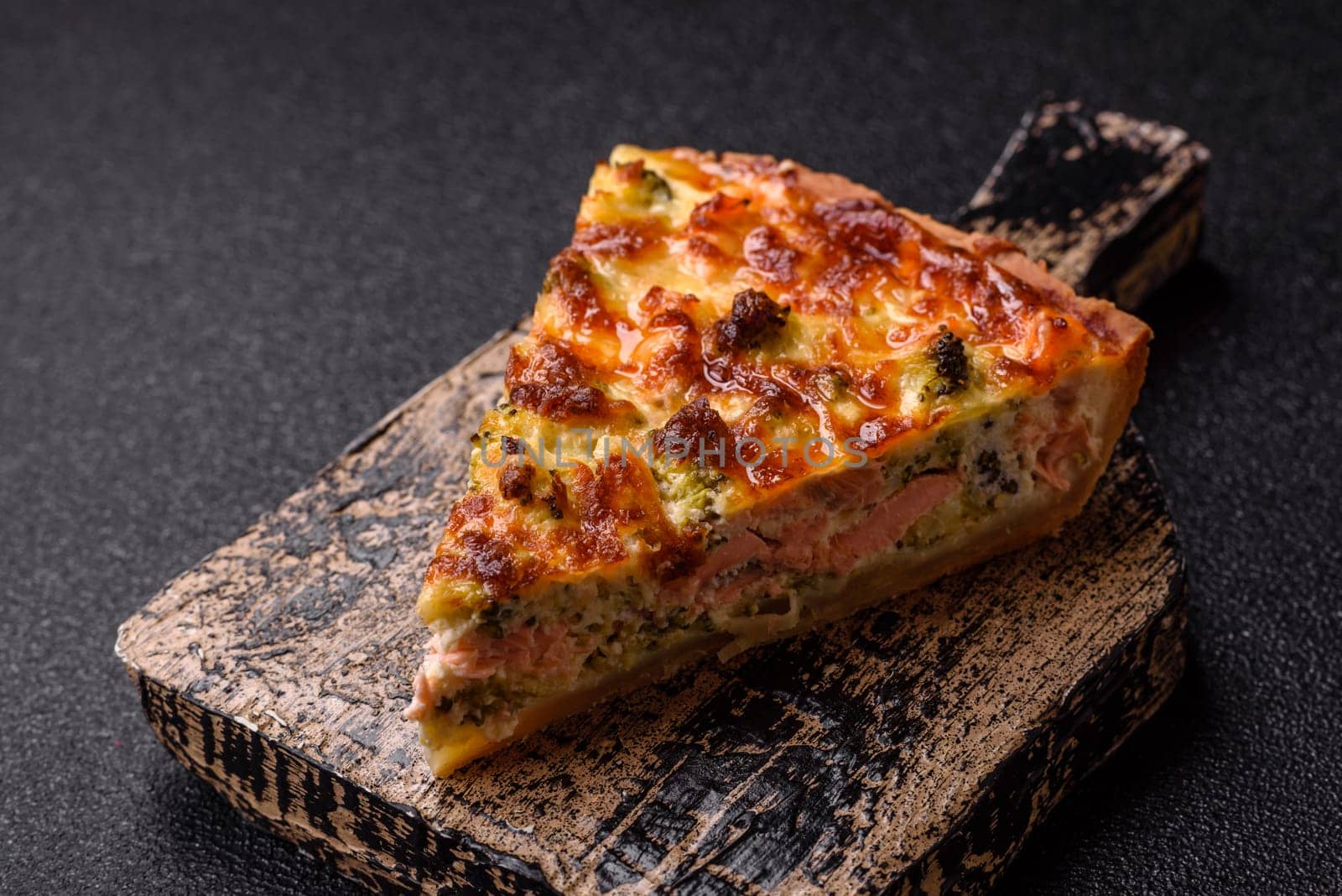 Delicious fresh quiche with broccoli, cheese, spices and herbs cut into pieces on a dark concrete background