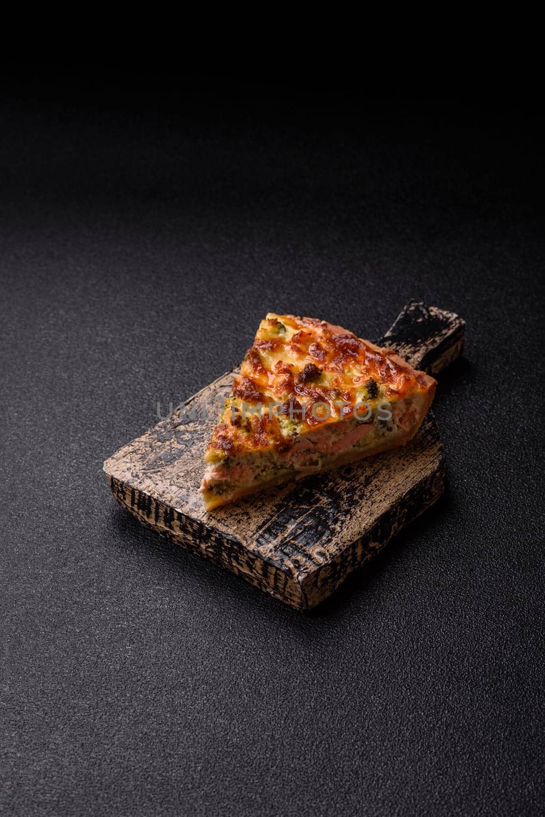 Delicious fresh quiche with broccoli, cheese, spices and herbs cut into pieces on a dark concrete background