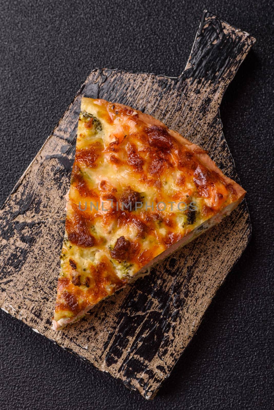 Delicious fresh quiche with broccoli, cheese, spices and herbs cut into pieces on a dark concrete background