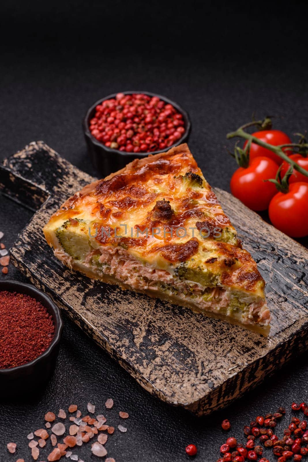Delicious fresh quiche with broccoli, cheese, spices and herbs cut into pieces on a dark concrete background