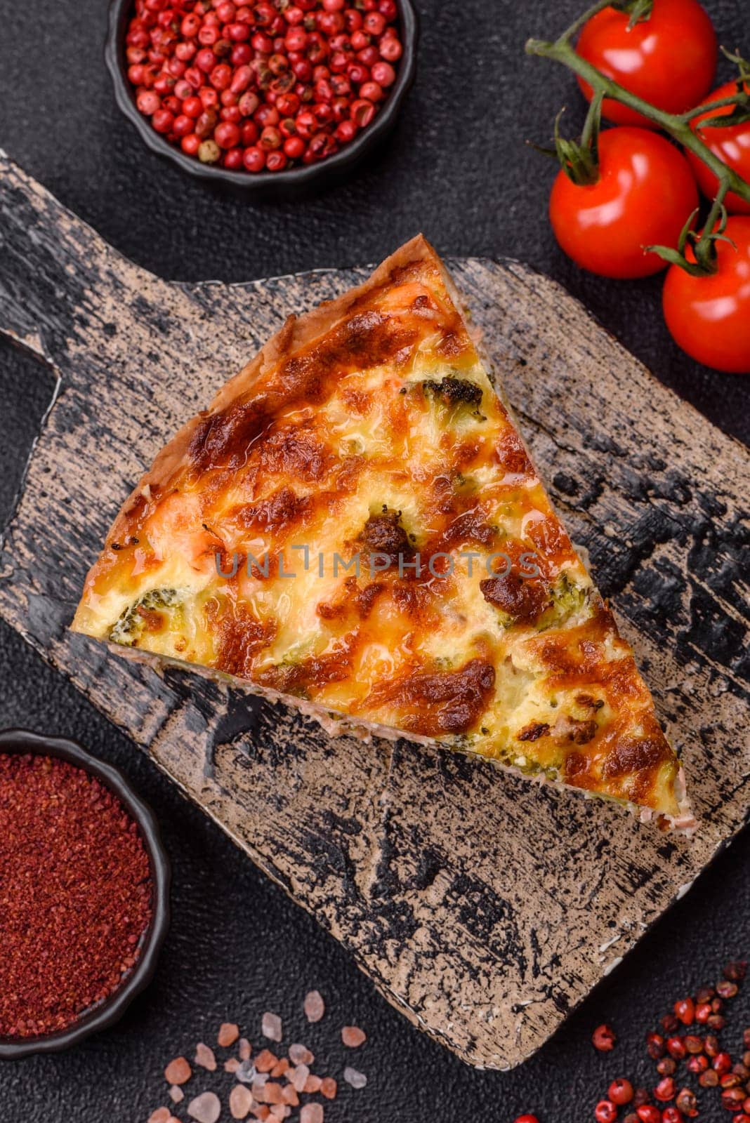 Delicious fresh quiche with broccoli, cheese, spices and herbs cut into pieces on a dark concrete background