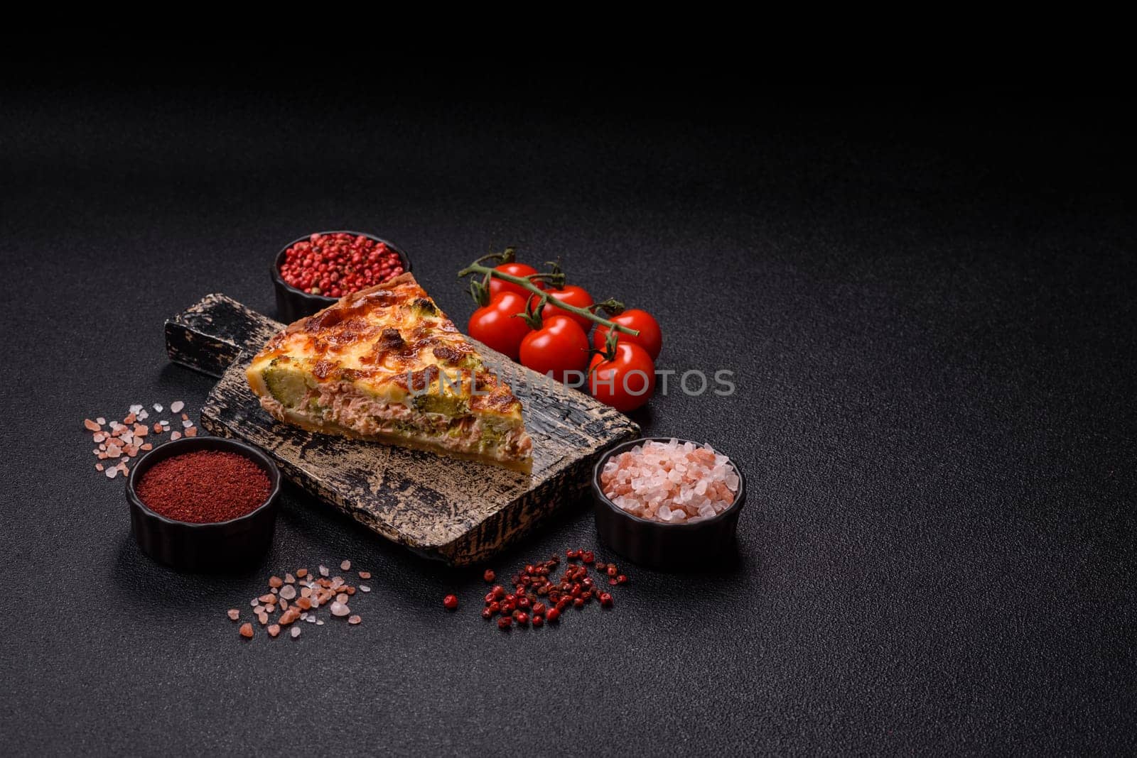 Delicious fresh quiche with broccoli, cheese, spices and herbs cut into pieces on a dark concrete background