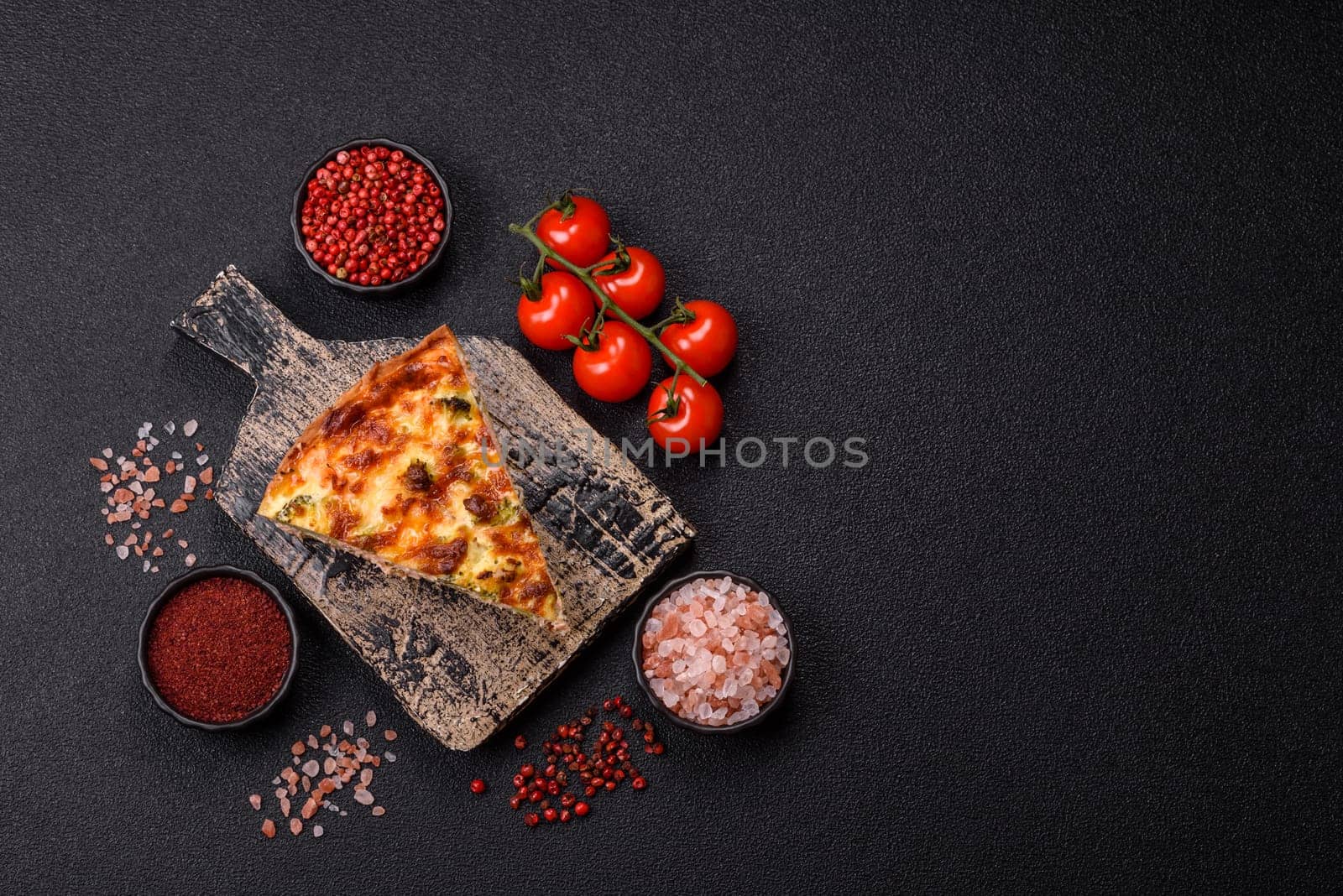 Delicious fresh quiche with broccoli, cheese, spices and herbs cut into pieces on a dark concrete background