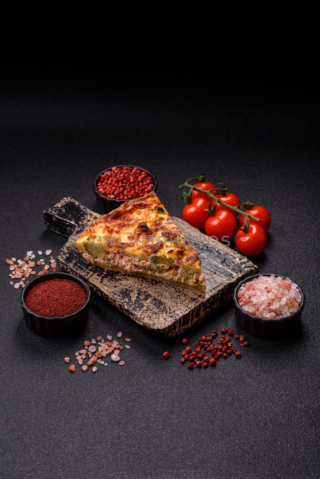 Delicious fresh quiche with broccoli, cheese, spices and herbs cut into pieces on a dark concrete background