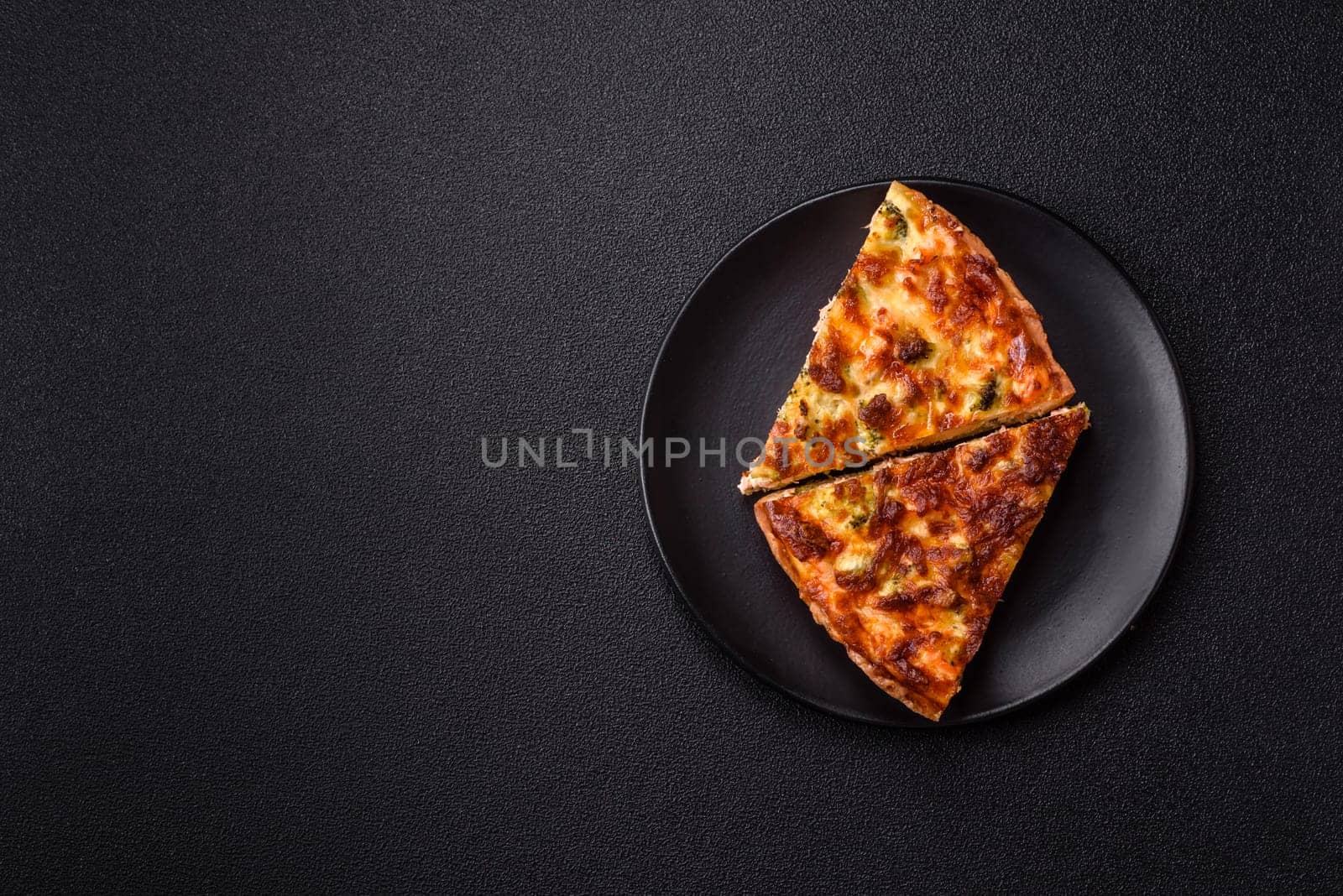 Delicious fresh quiche with broccoli, cheese, spices and herbs cut into pieces on a dark concrete background