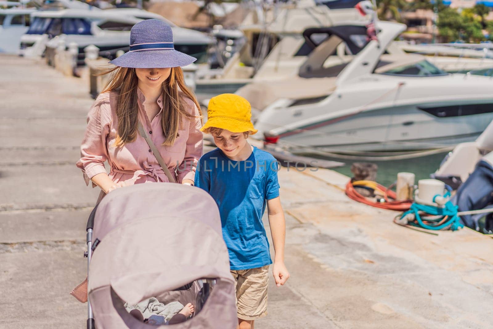 A mother and her elder son enjoy a peaceful walk along the waterfront, pushing a baby stroller with their youngest family member. A heartwarming moment of family bonding, parenting, and outdoor leisure.