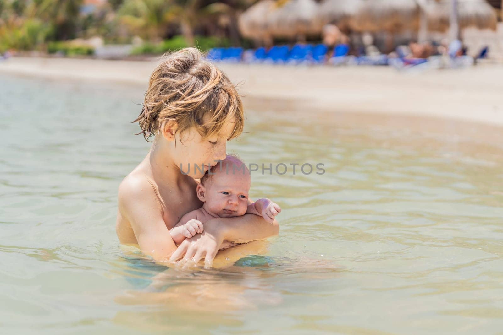 An older brother gently holds his baby sibling while swimming in the sea, sharing a joyful and heartwarming moment of family bonding and summer fun in the water. A perfect blend of love, care, and childhood adventure.