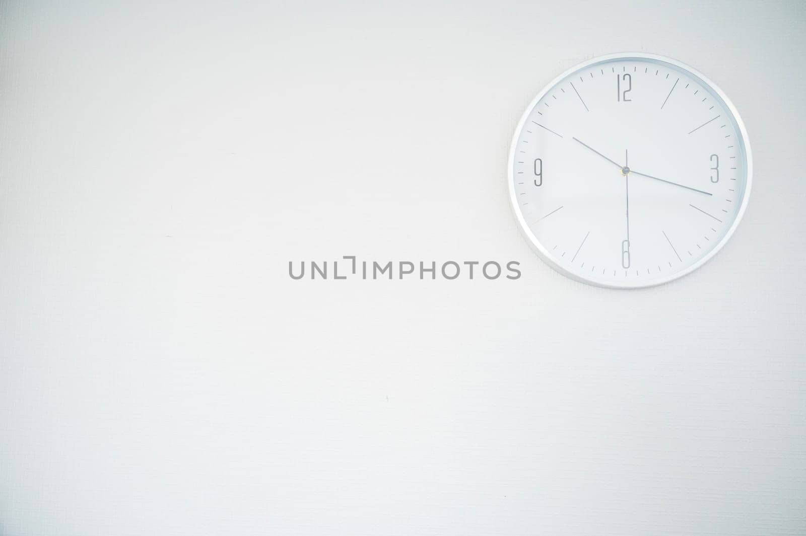 white round clock on a white wall. the clock is located in the upper right part. space for an inscription. the clock shows 10.18