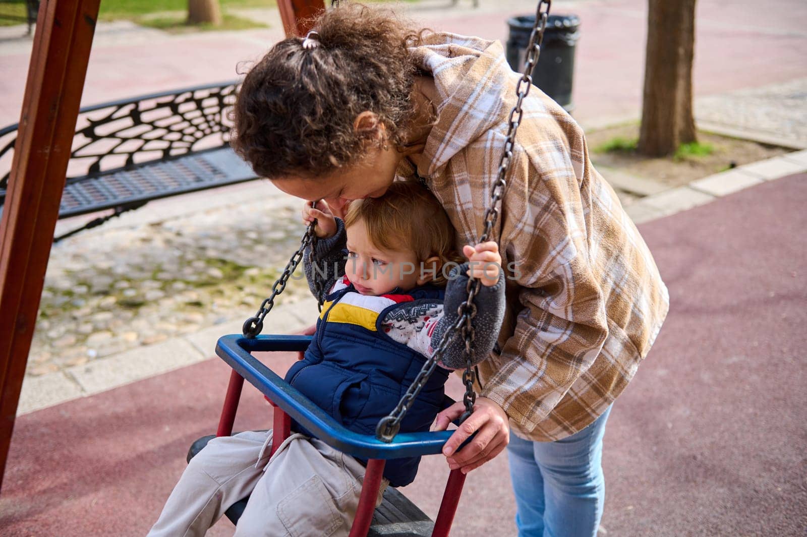 A mother enjoys a joyful moment with her young child, bonding as they play on a swing in a serene park setting, showcasing familial love, care, and outdoor activities.