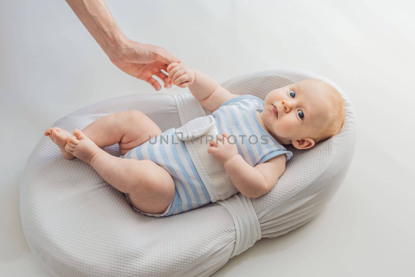 Adorable 3-month-old baby lying safely in a cozy infant cocoon secured with a special safety belt. Comfortable and protective design for newborn care. Parenting, safety, and baby comfort concept.
