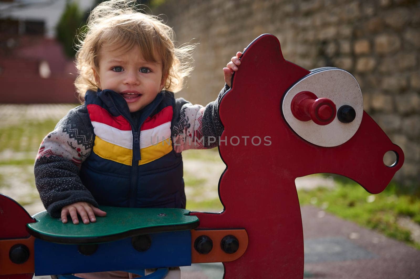 A cheerful toddler enjoying their time outside while playing on a large playground toy shaped like a horse. The sunny day highlights the child's joyful expression and the vibrant colors of the equipment.