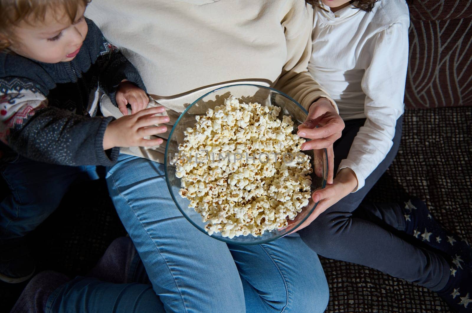 A close-up view of a family sitting together and sharing a bowl of popcorn, highlighting cozy bonding and quality time spent during leisure moments. Suitable for themes of family, togetherness, and happiness.