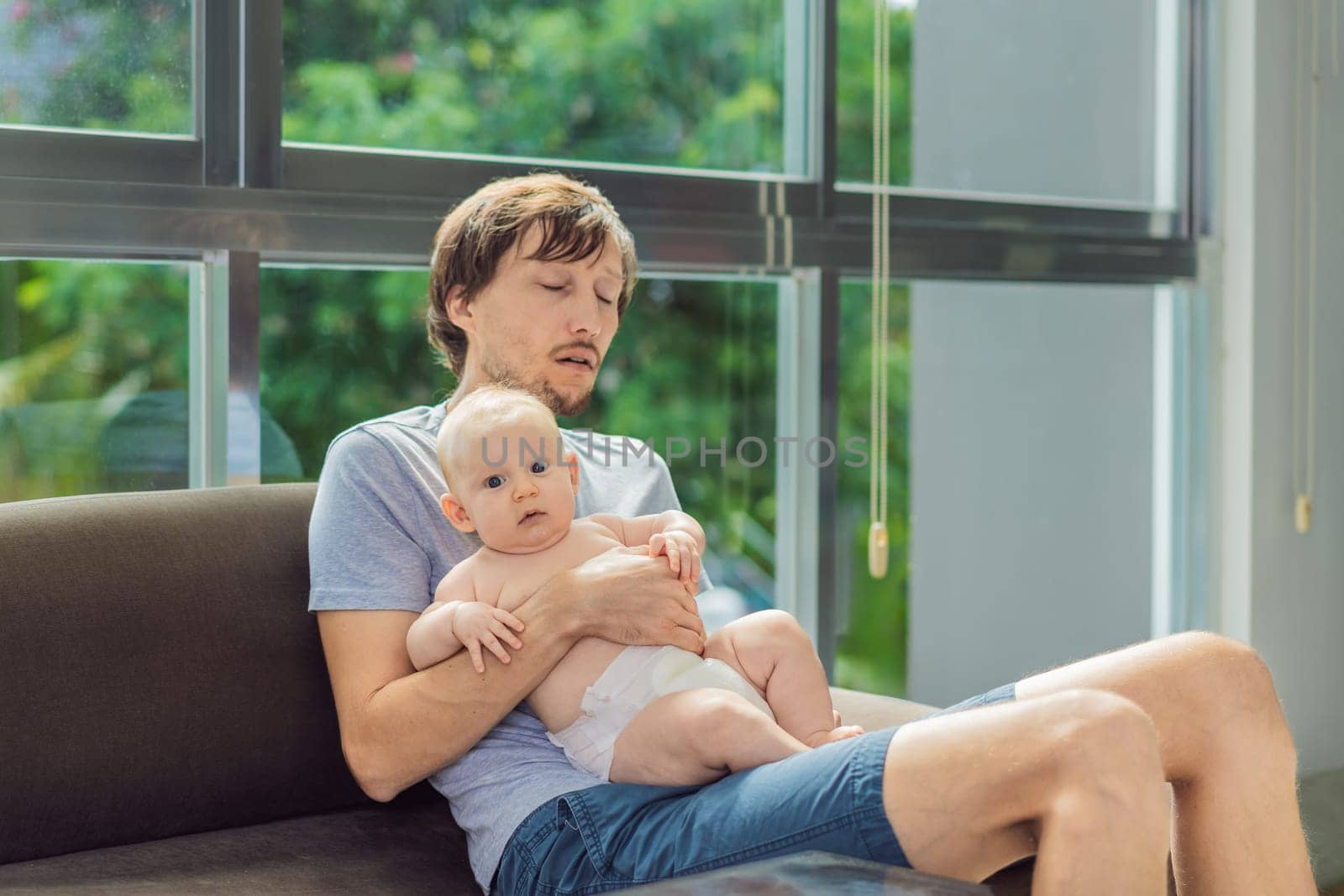 An exhausted father falls asleep on the couch while holding his 3-month-old baby in his arms. A tender and heartwarming moment showcasing love, caregiving, and the challenges of parenthood. Family and bonding concept.