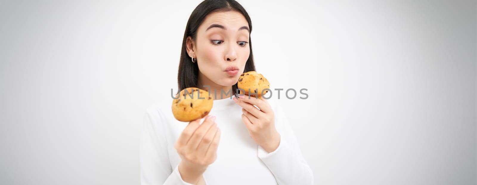 Close up portrait of asian girl eats cupcakes with happy face, isolated on white background.