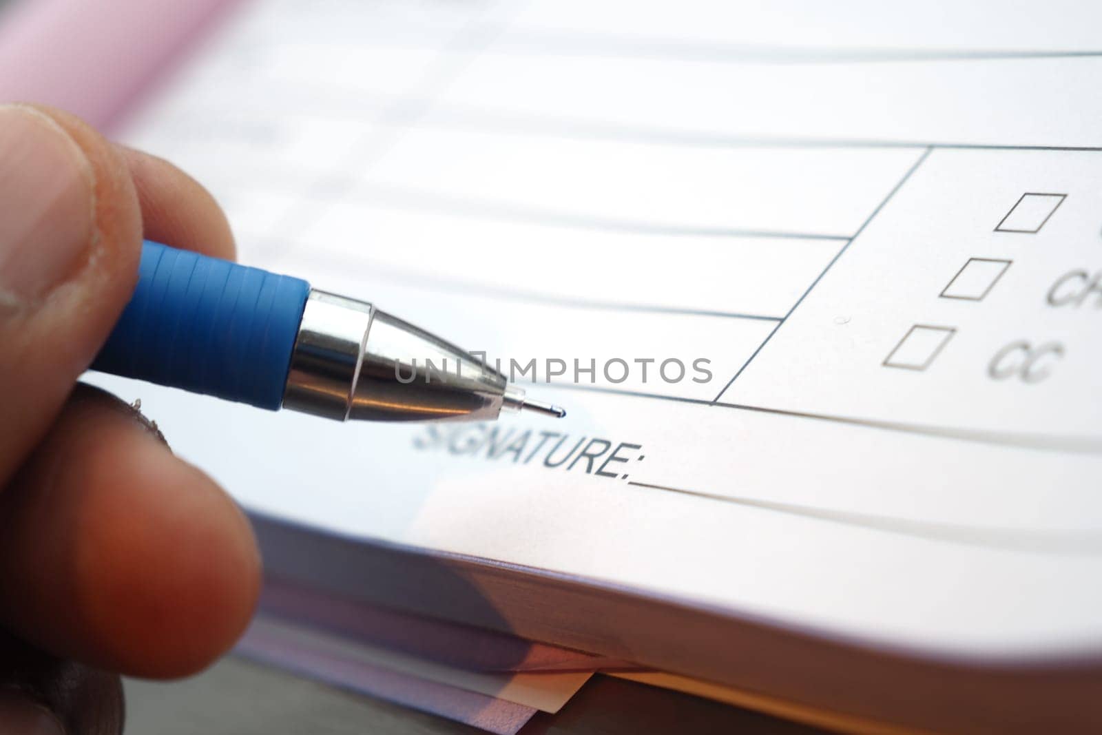 A hand is using a blue pen to sign a document with checkboxes.