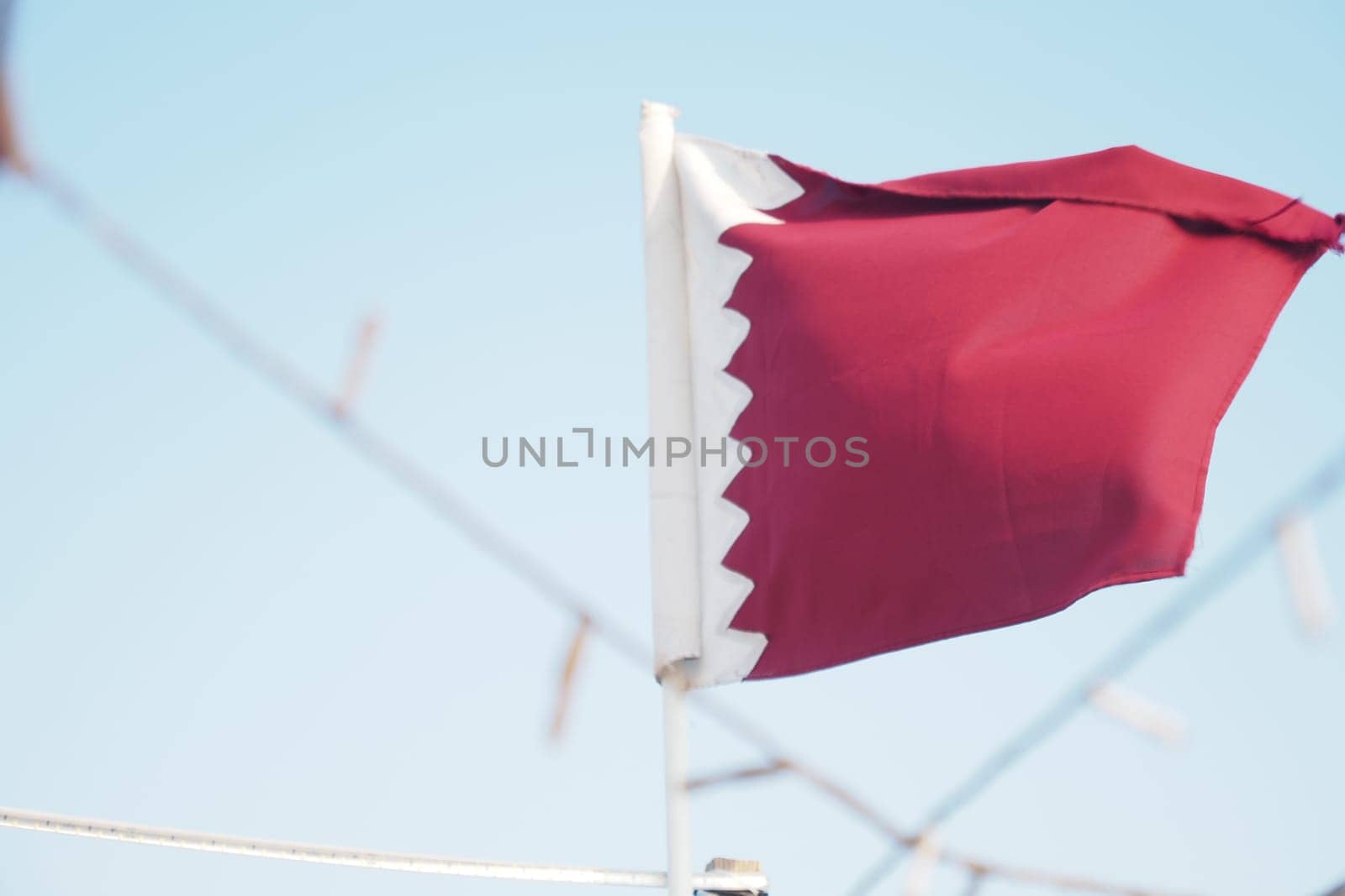 A vibrant flag of Qatar flutters in the breeze on a sunny day.