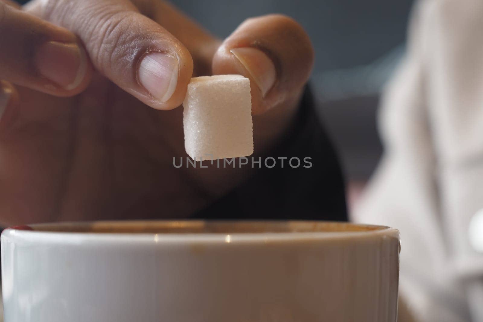 A hand gently places a sugar cube into a warm drink at a cafe.