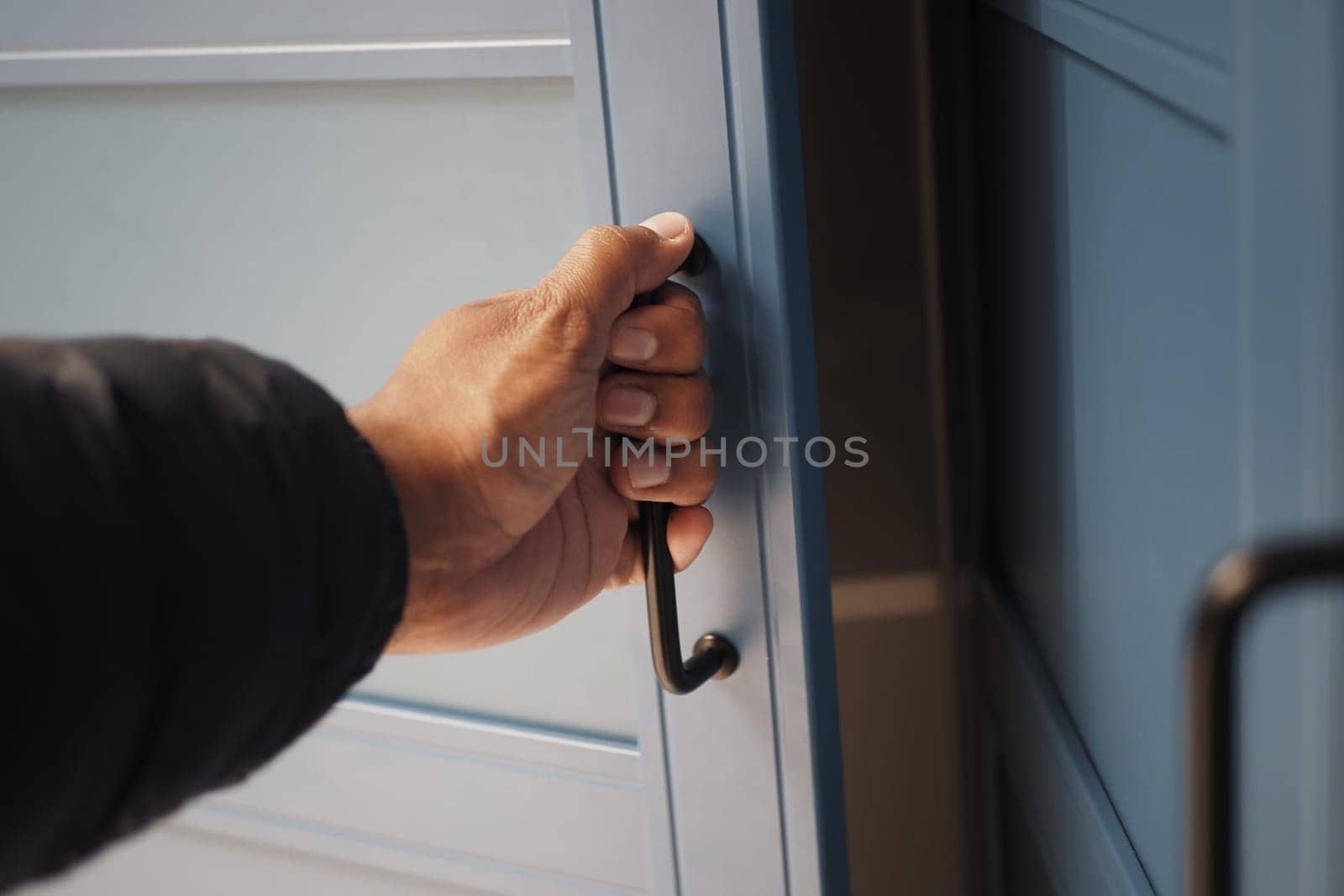 A person grips the handle of a blue cabinet door indoors, prepared to open it.