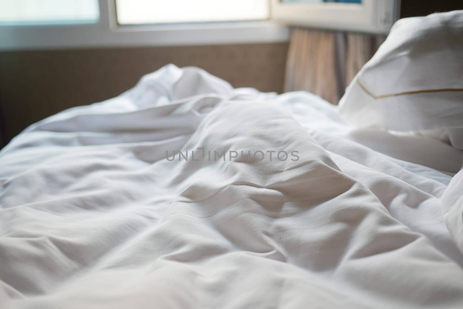 Crumpled white sheets lie on a cozy bed under warm sunlight.