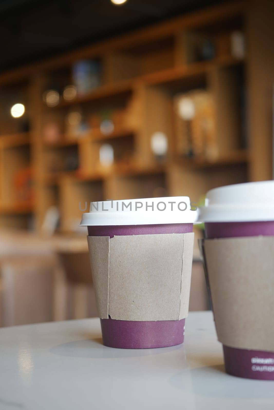 Two coffee cups sit on a table in a warm, inviting cafe atmosphere.