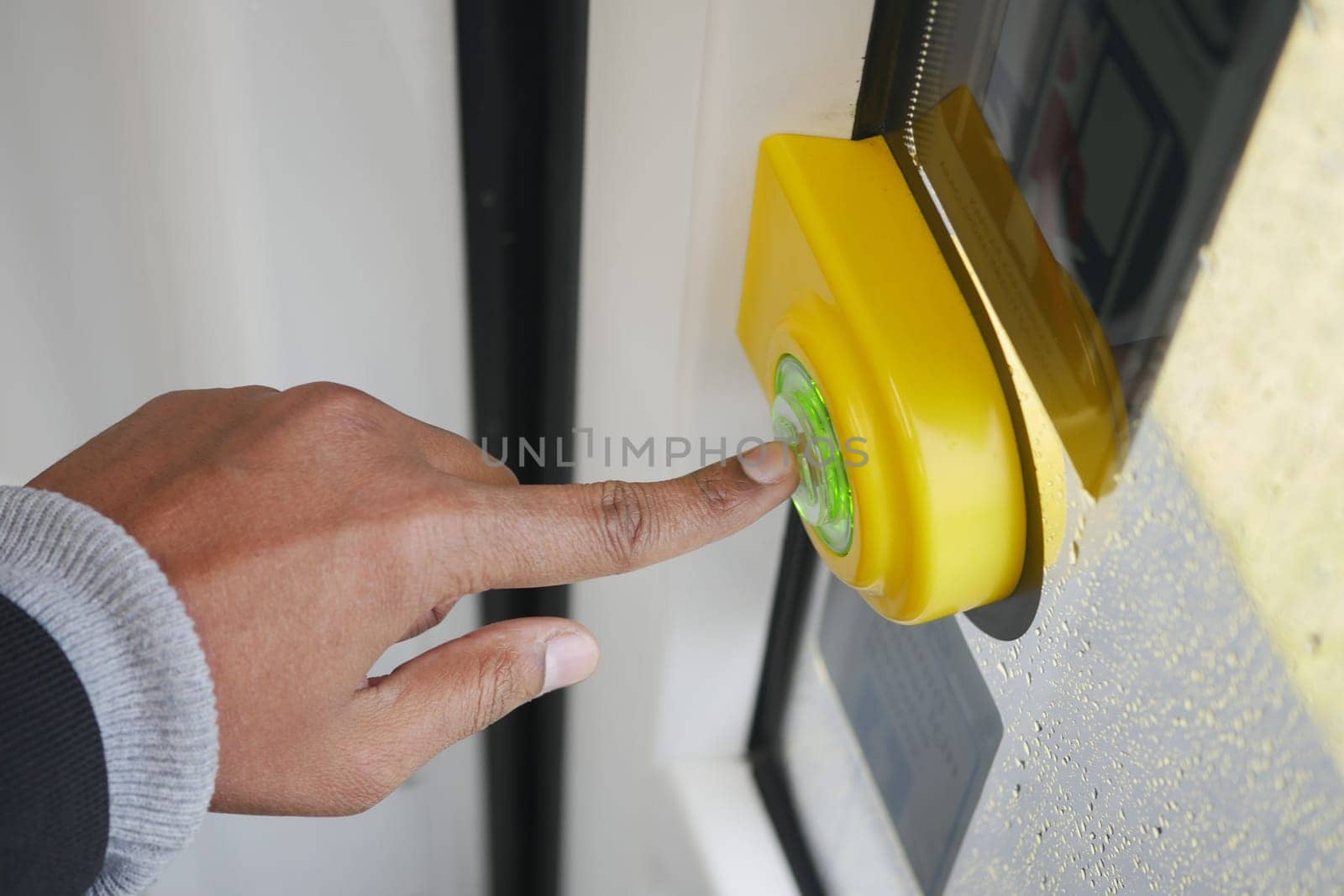 Individual activates a bright green bus stop button on a rainy day.