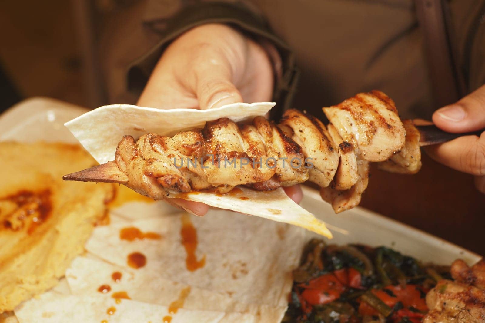 Person enjoys a grilled chicken skewer on a tortilla in a cozy setting.