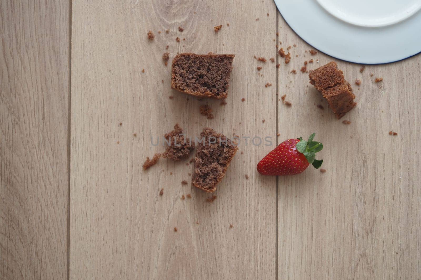 An image depicting a fallen plate on a floor with chocolate dessert pieces and a strawberry.