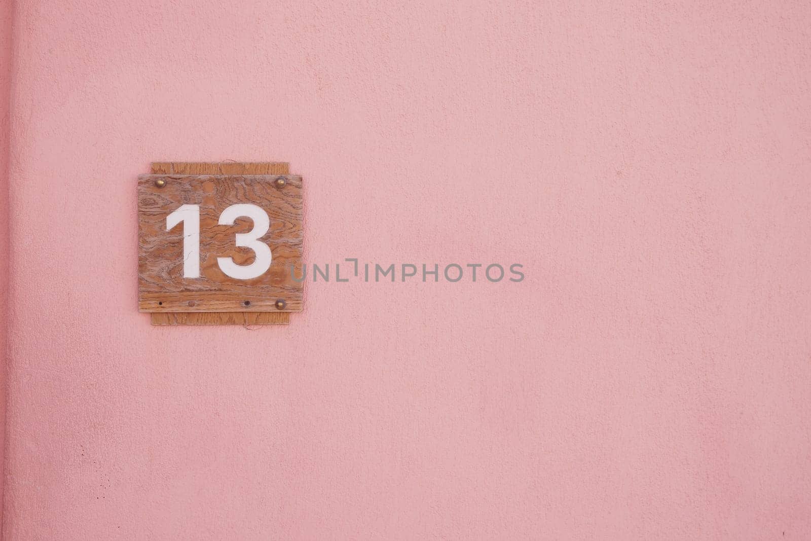 House number thirteen displayed on a pink wall under bright sunlight.