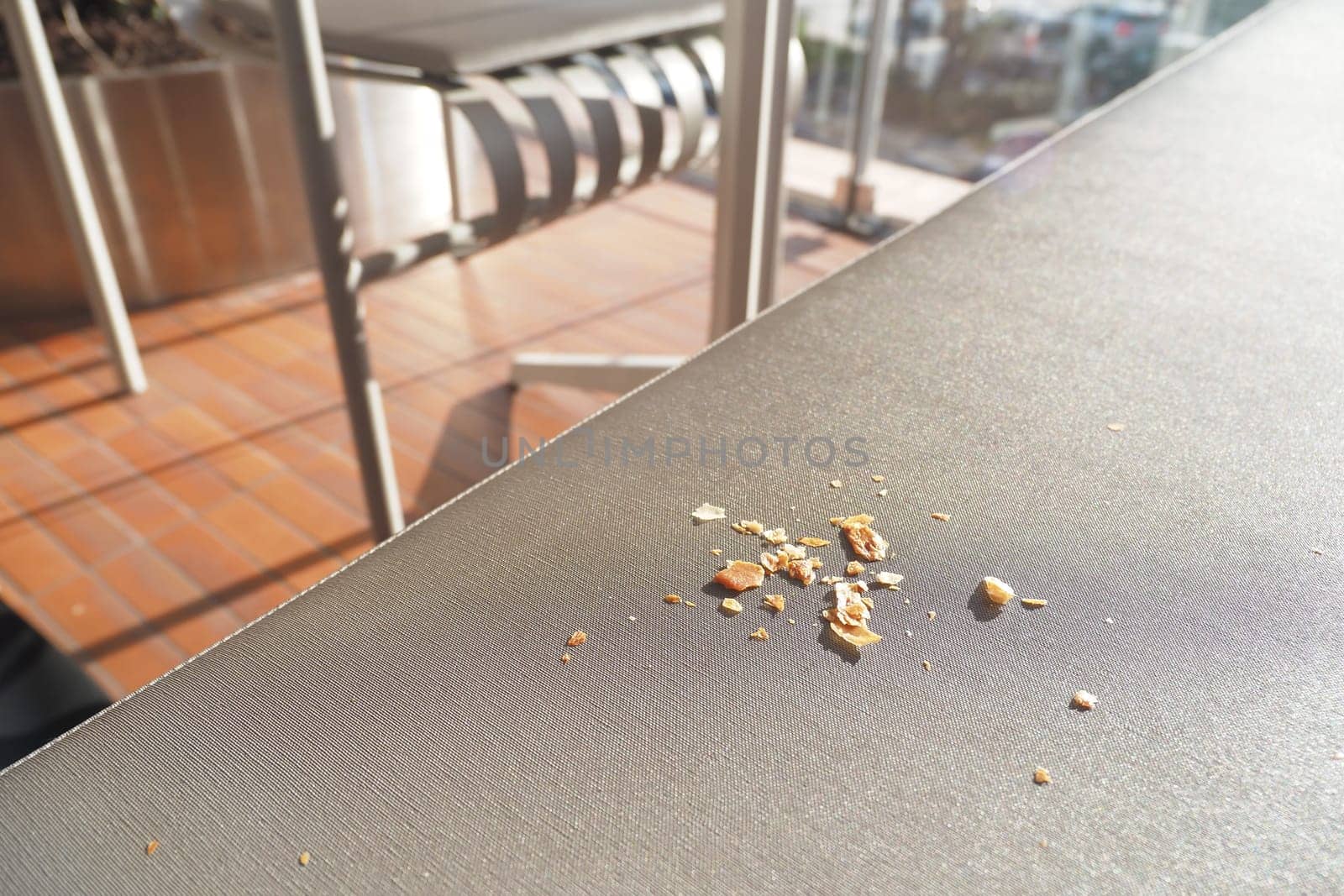 Small pieces of food litter a sunlit outdoor table setting.