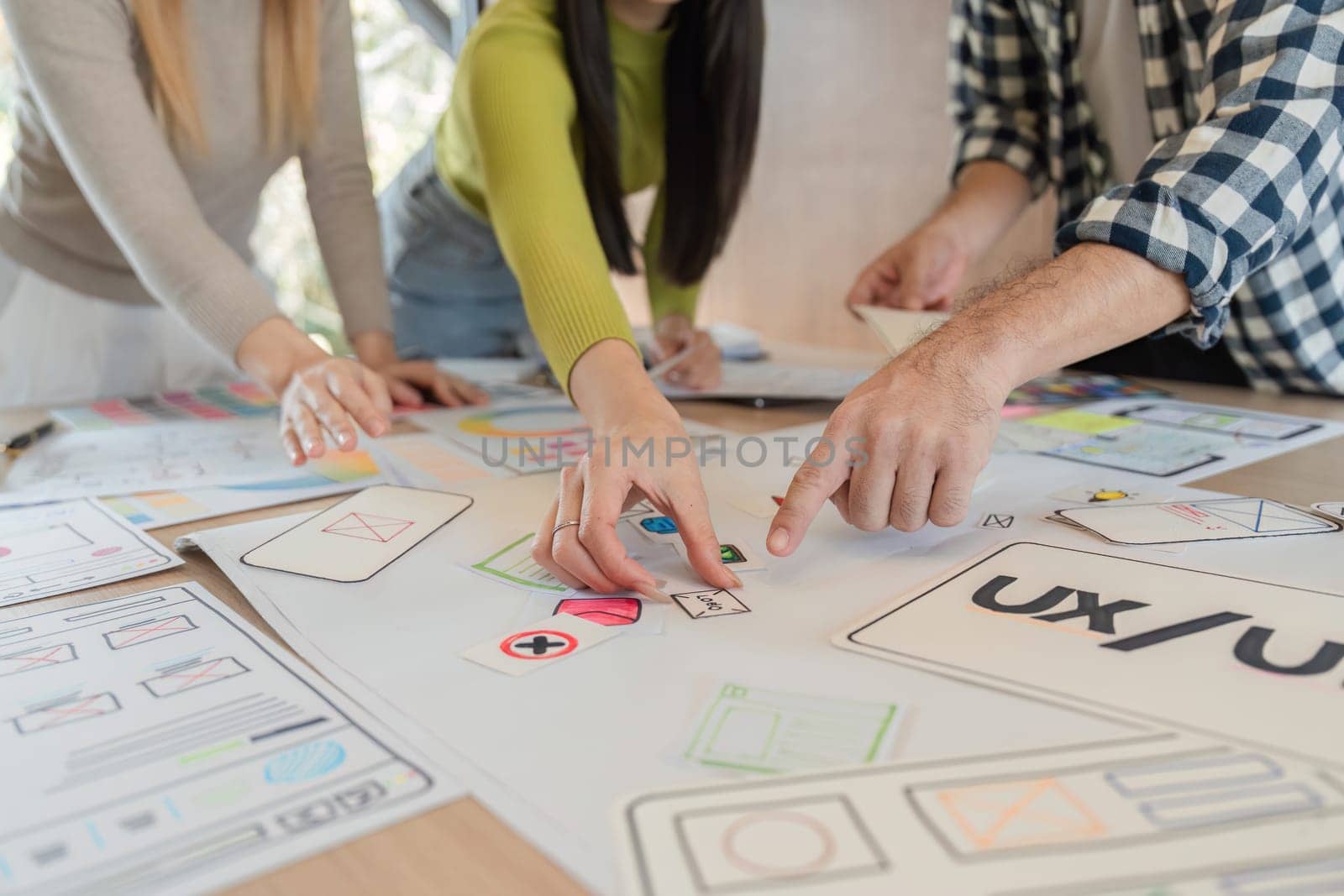 A diverse group of team members analyzing UXUI design prototypes and providing feedback during a collaborative brainstorming session at a modern office table.