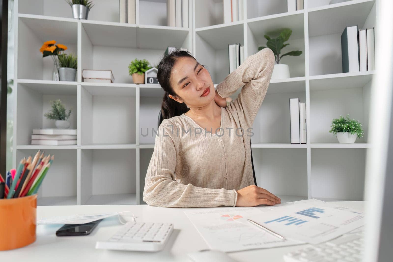 A woman stretching her neck to relieve discomfort while working at her desk, illustrating the effects of office syndrome in a professional setting.