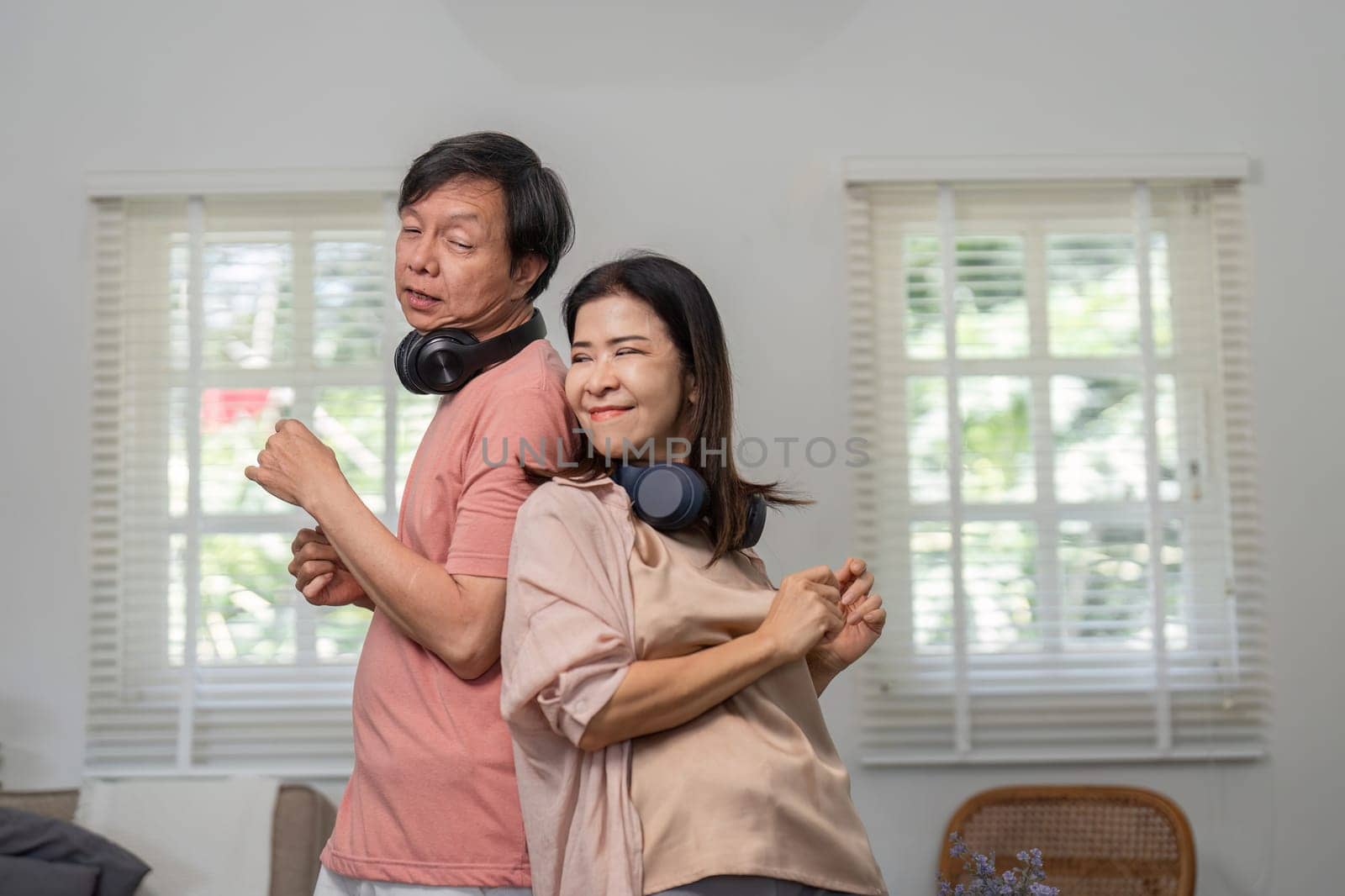 A joyful diverse couple dances back to back, enjoying music with headphones in their comfortable home setting.
