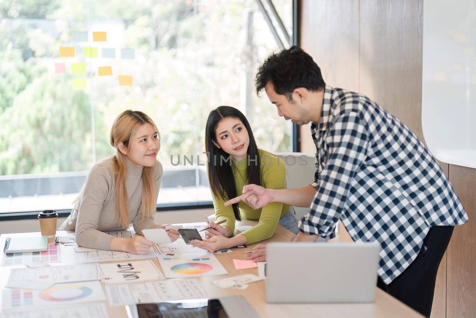 A diverse team engaged in a vibrant discussion about design concepts while reviewing materials at a table in a contemporary office space.