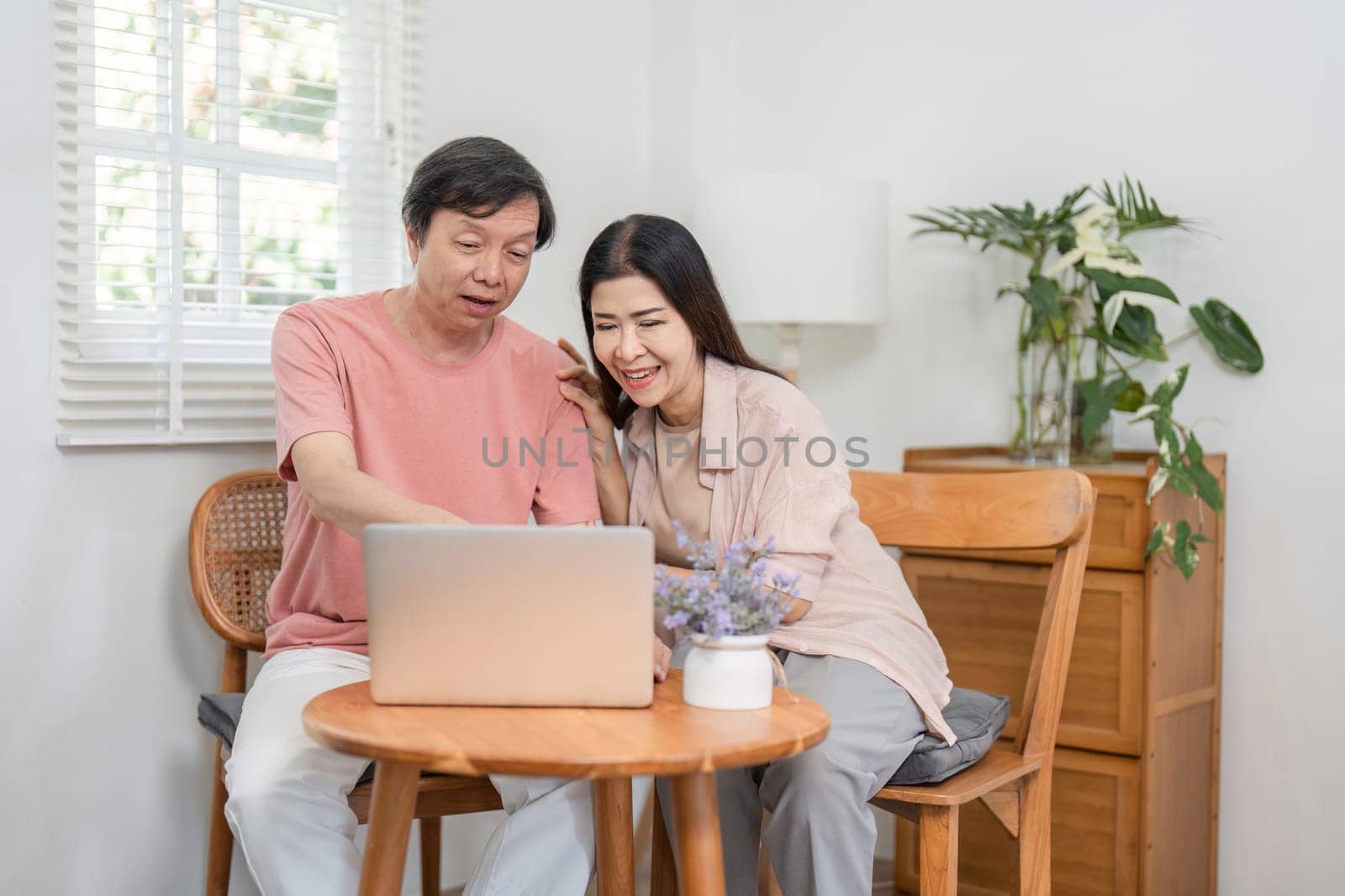 A diverse older couple engaged in online activities together, smiling while using a laptop at their cozy home.