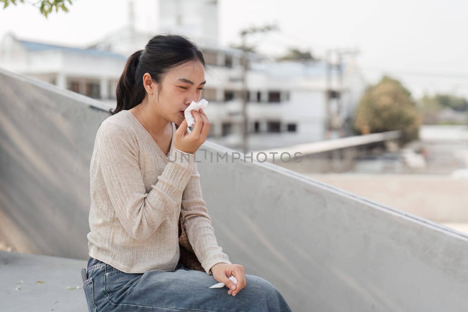 A diverse woman wearing a mask, wiping her tears while sitting outdoors in a city setting, displaying vulnerability.