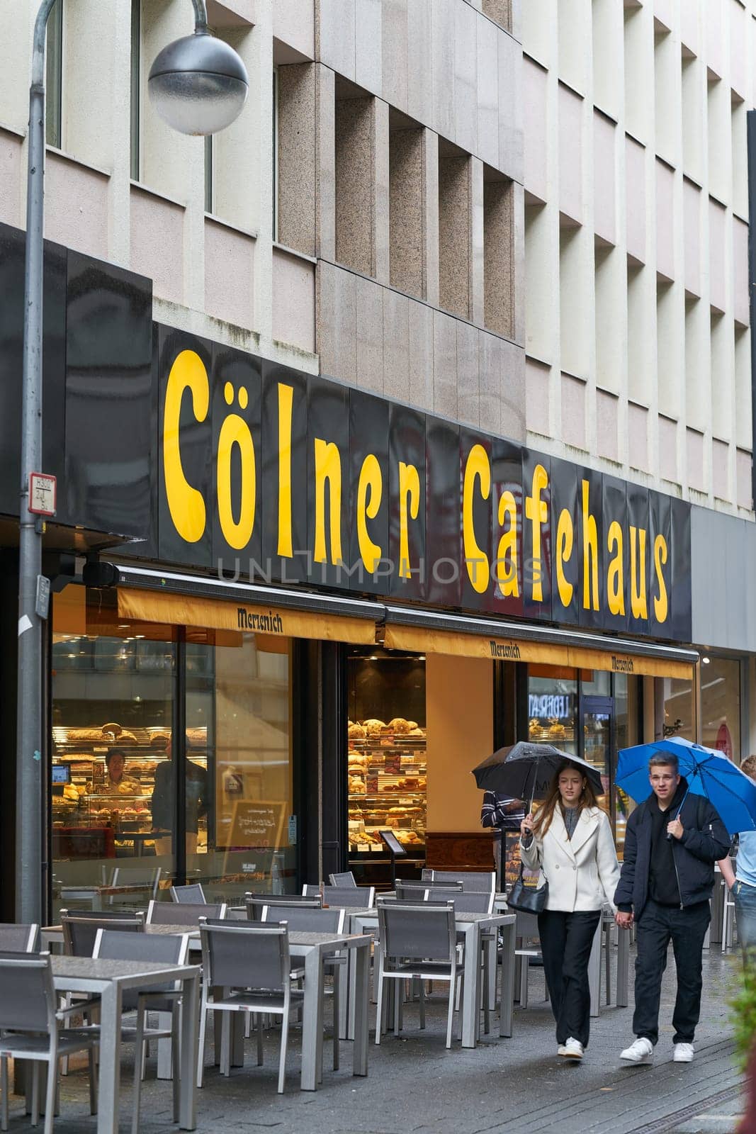 Cologne, Germany – May 24, 2024: Cologne city center with walkers in front of a café in rainy weather