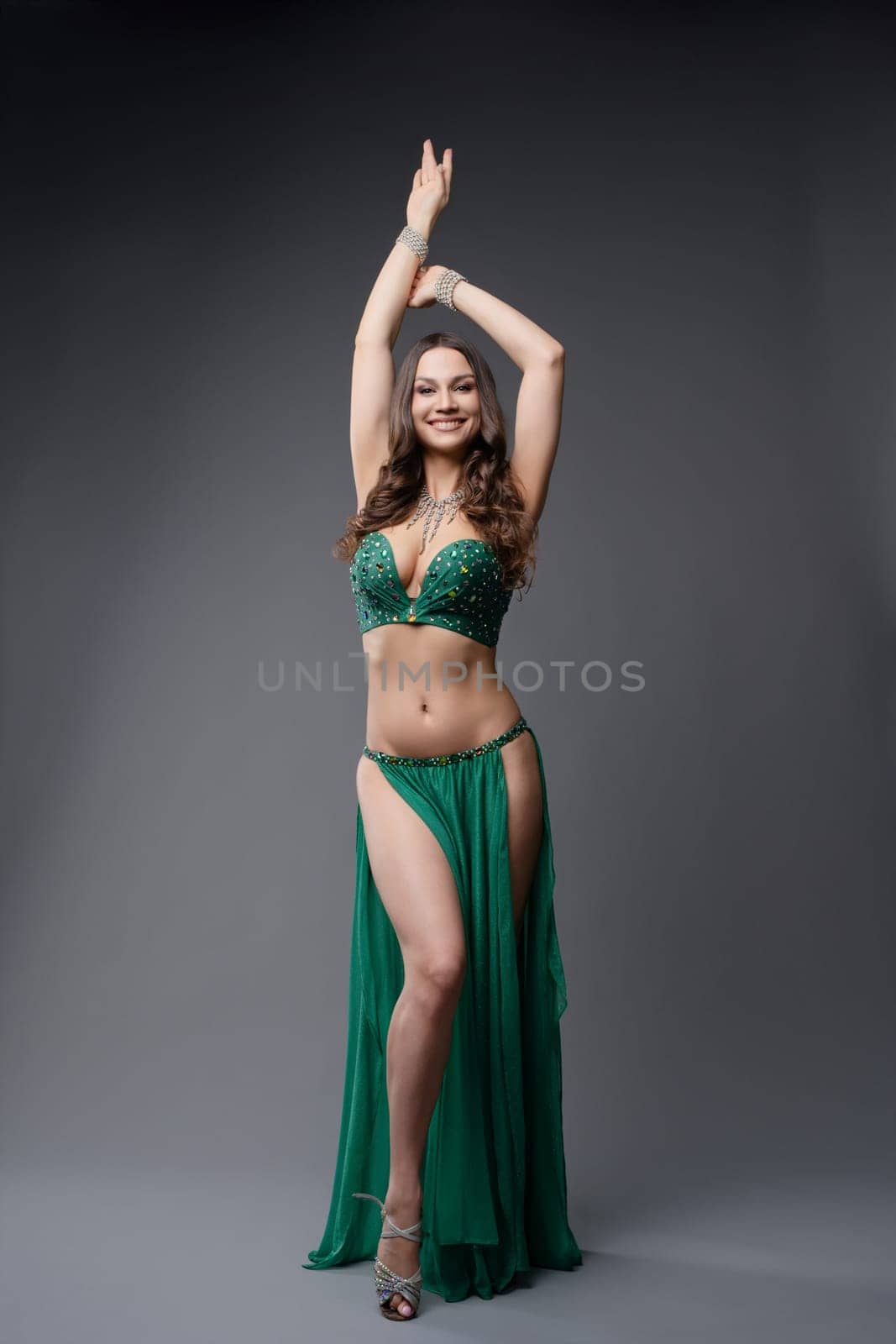 A skilled belly dancer showcases her talent, dressed in a stunning green costume, while posing gracefully in a studio environment.