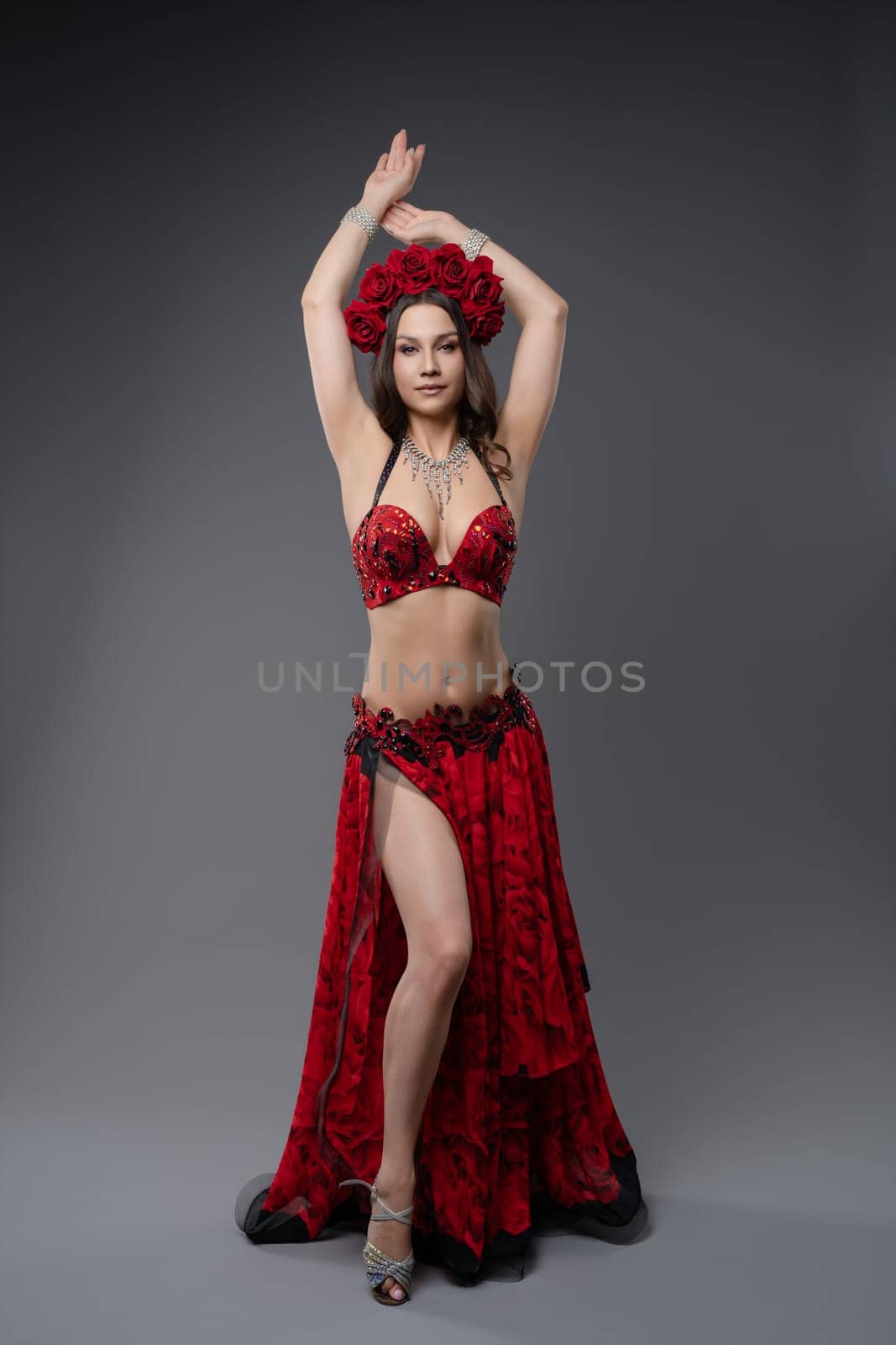 A graceful dancer showcases her skills in a stunning red outfit adorned with flowers, performing artfully against a neutral backdrop.