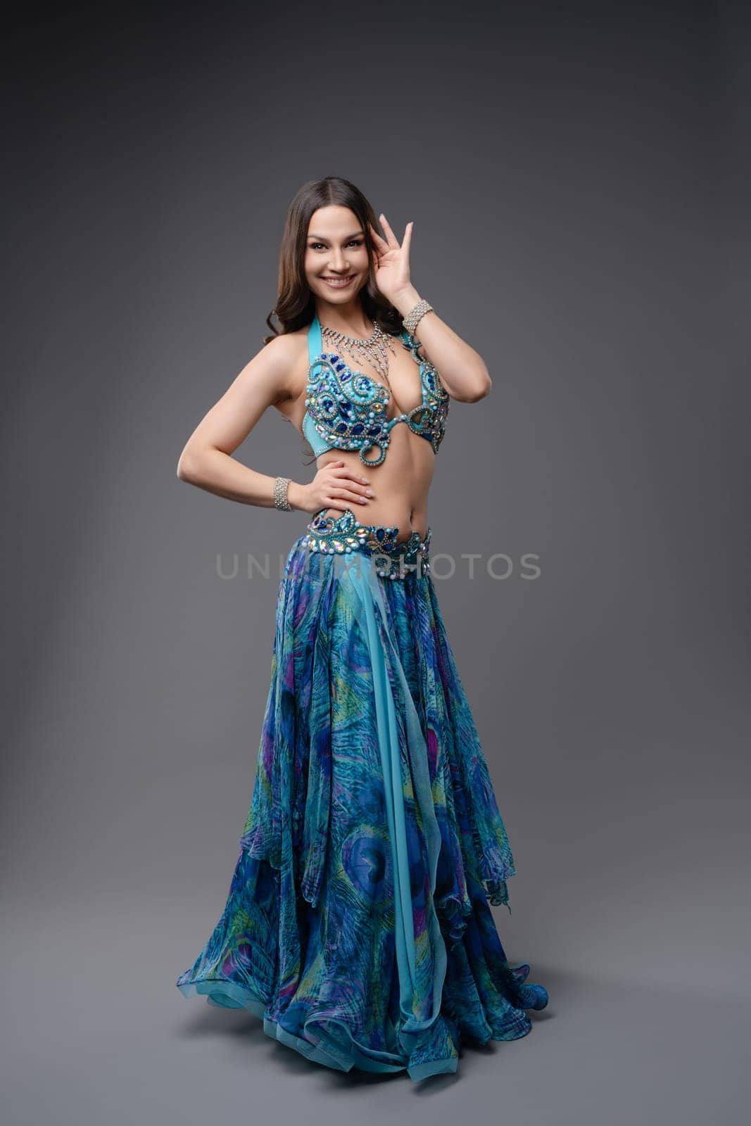 A talented dancer poses gracefully in a stunning blue costume, showcasing intricate details and accessories in a studio setting.