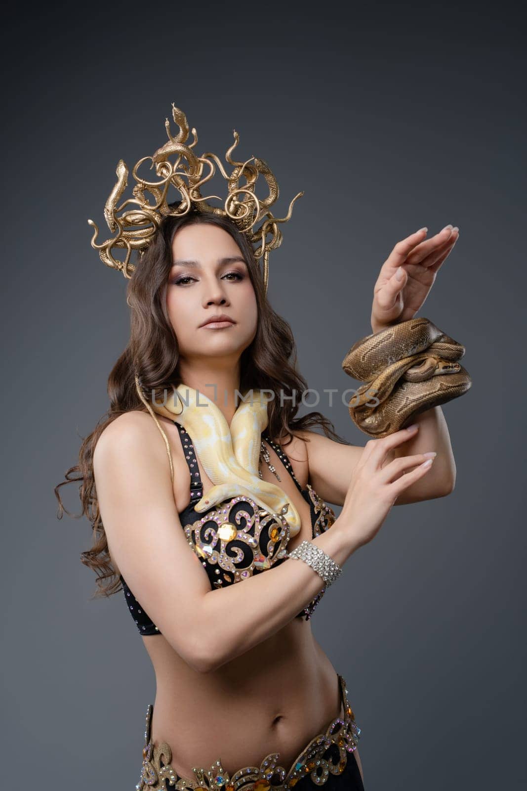 A dancer performs with a snake draped around her arm in an artistic studio. Her elegant attire enhances the captivating display of movement.