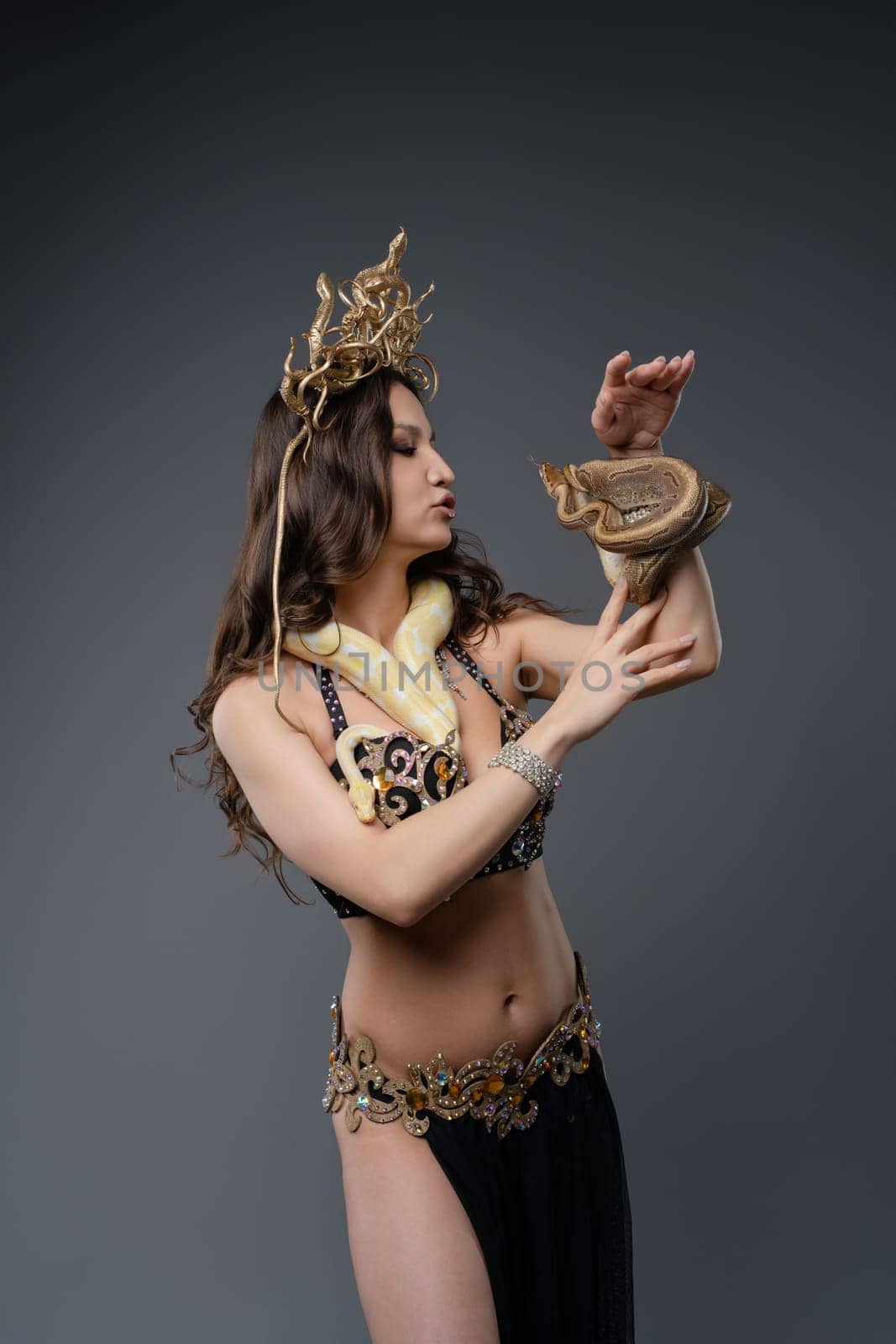 A dancer adorned in shimmering attire interacts gracefully with a snake, highlighting an artistic performance in a well-lit studio.