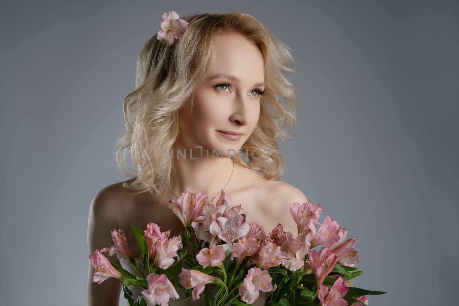 A female model stands elegantly in a studio, holding a vibrant bouquet of flowers and wearing a soft expression, surrounded by a neutral background.
