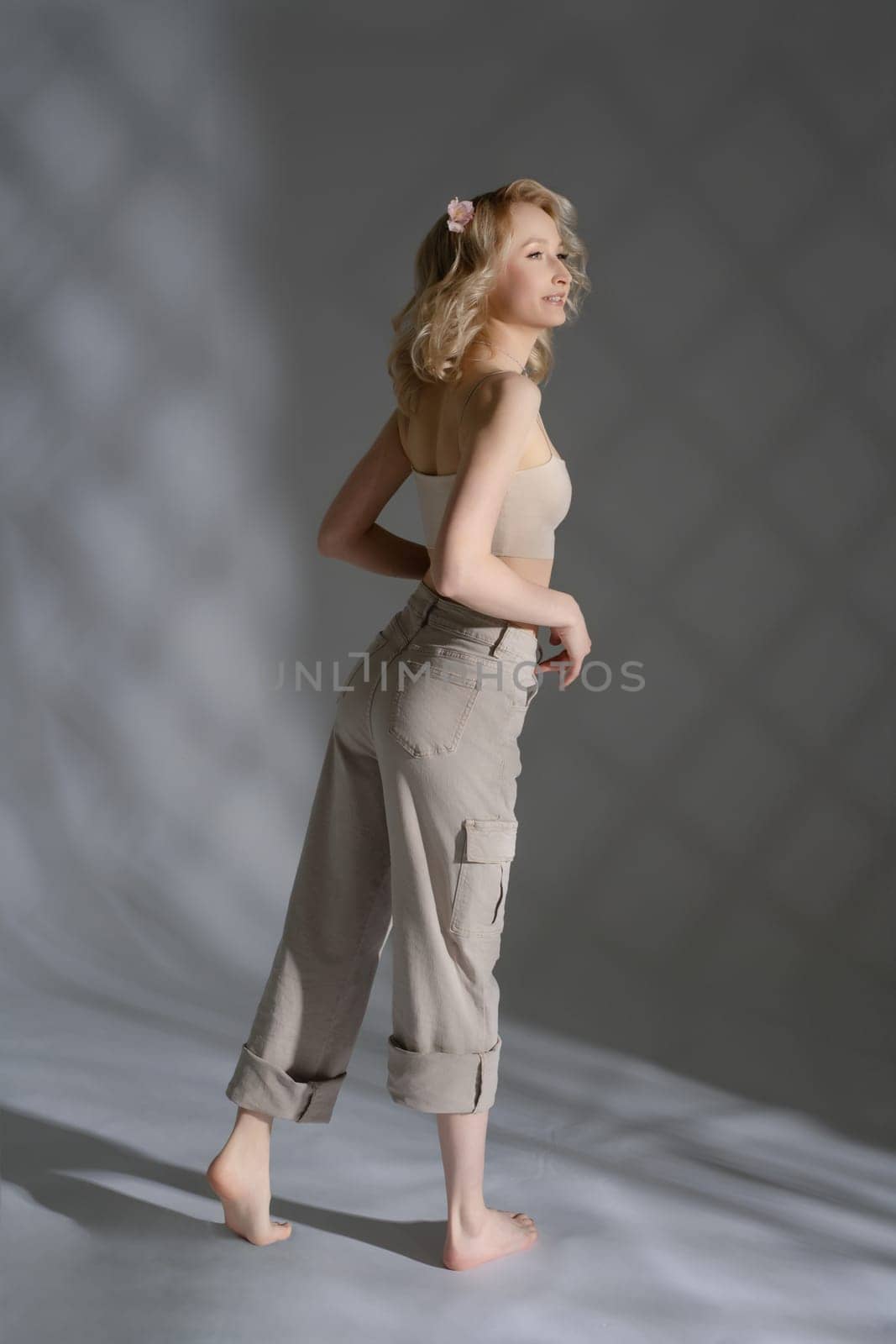 A young woman stands barefoot, showcasing a casual outfit in soft lighting, creating a serene and artistic atmosphere.