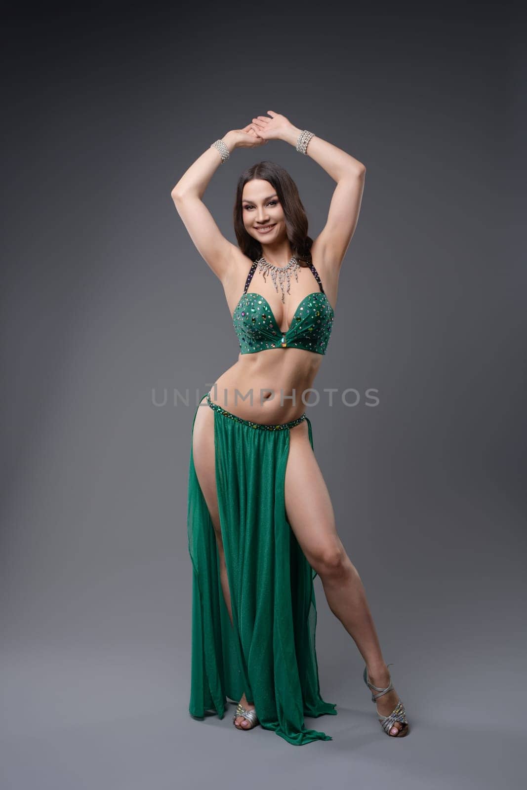 A skilled belly dancer showcases her talent in a vibrant green costume, displaying intricate movements in a studio.